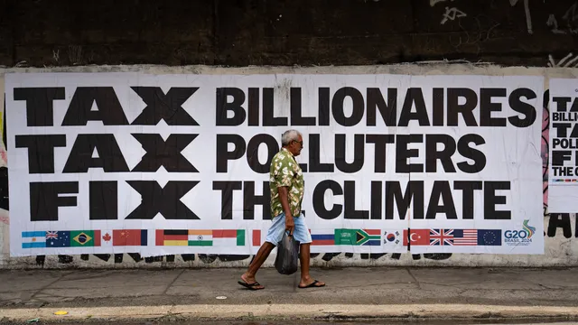 A person walks past a large protest banner reading "TAX BILLIONAIRES TAX POLLUTERS FIX THE CLIMATE" with G20 country flags displayed below. The sign advocates for climate action through taxation of the wealthy.