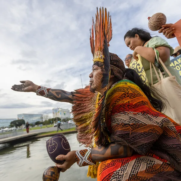 Indigenous protesters in traditional dress and feathered headdress doing an action in a public city space.