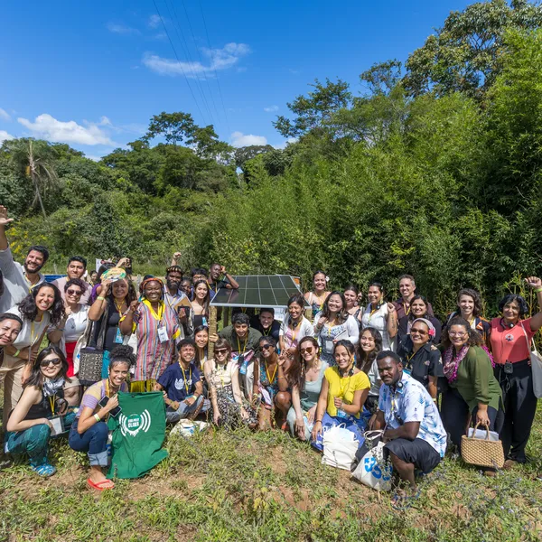Large group of activists posing with solar pannel amongst trees.