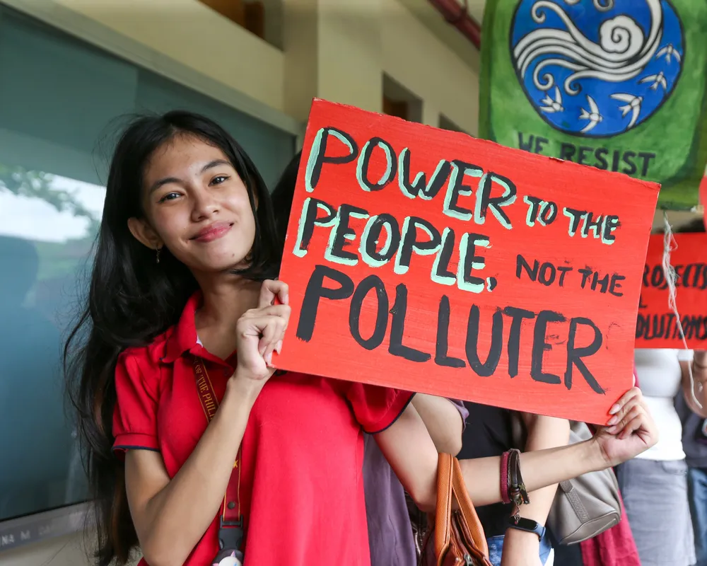 A young student stands with a poster saying power to the people, not the pollutor.
