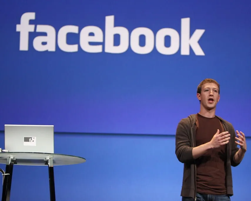 Picture of Mark Zuckerberg next to podium in front of Facebook logo on blue background