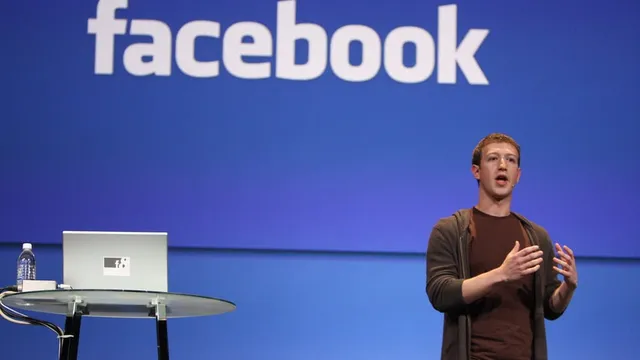 Picture of Mark Zuckerberg next to podium in front of Facebook logo on blue background
