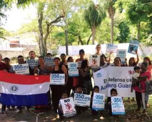 Community group holding protest signs and Paraguayan flag outdoors under trees, advocating for the Chaco Guasu forest with "350.org" placards displayed by participants of various ages.