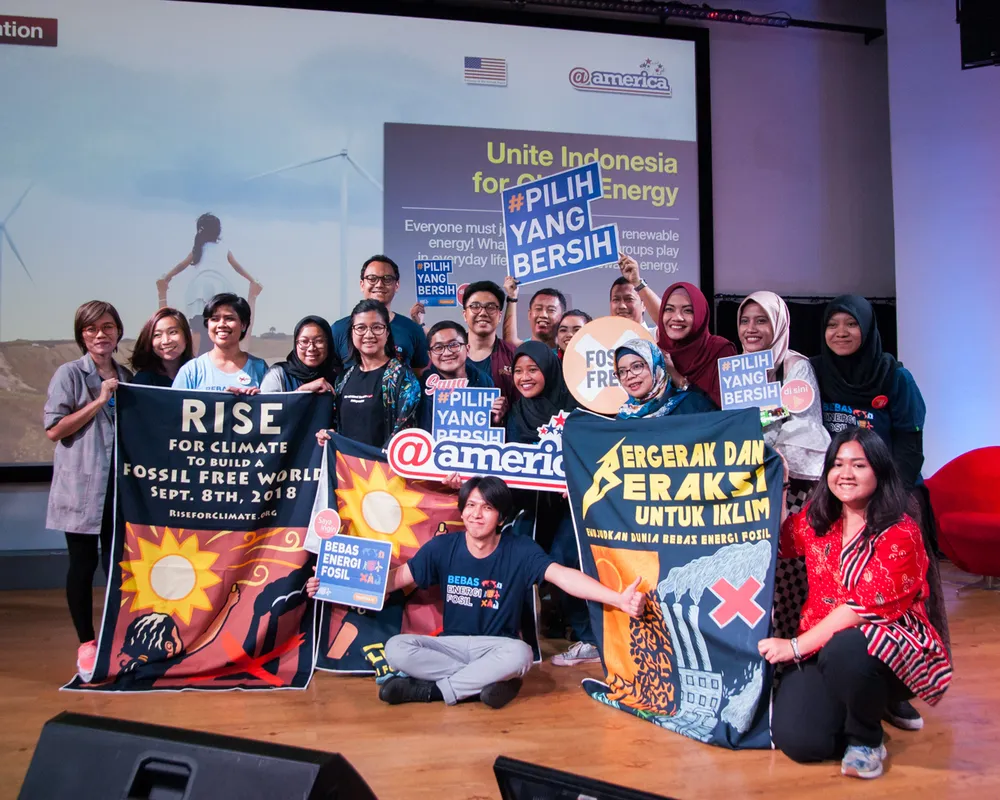 A group of climate activists in Indonesia poses with banners promoting renewable energy and fossil fuel-free future. They hold signs advocating for clean energy choices during a presentation event about sustainable energy.