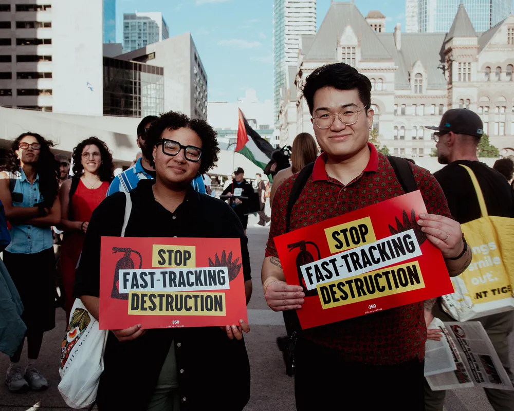 A portrait of two people holding signs that read "Stop Fast-Tracking Destruction"