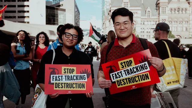 A portrait of two people holding signs that read "Stop Fast-Tracking Destruction"