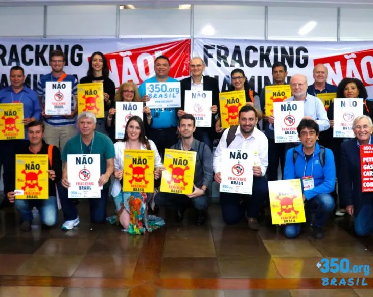 Group of activists protesting fracking in Brazil, holding "NÃO" (NO) signs with skull symbols and anti-fracking banners. Part of 350.org Brasil environmental campaign against hydraulic fracturing.