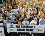 Protest march with crowd holding banner reading "NÃO QUEREMOS O GÁS DA MORTE" (We Don't Want Death Gas). Demonstrators gathered on street advocating against gas use or distribution.