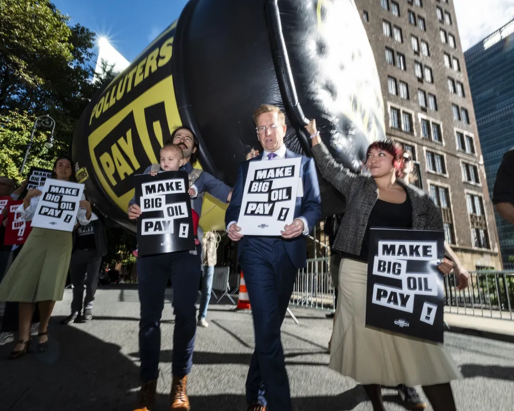 Climate activists protest outside UN headquarters with giant inflatable wrecking ball and "Make Big Oil Pay" signs, demanding fossil fuel companies fund climate action and bear responsibility for environmental damage.