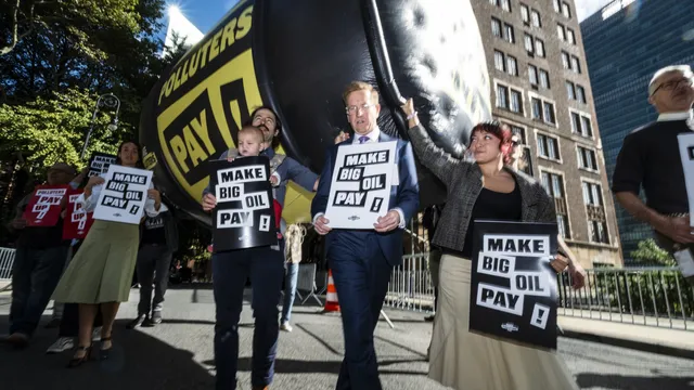 Climate activists protest outside UN headquarters with giant inflatable wrecking ball and "Make Big Oil Pay" signs, demanding fossil fuel companies fund climate action and bear responsibility for environmental damage.