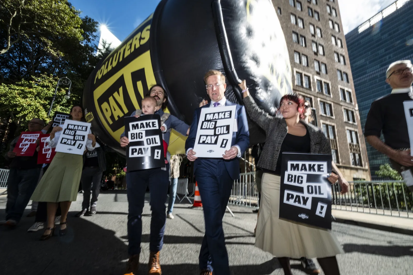 Climate activists protest outside UN headquarters with giant inflatable wrecking ball and "Make Big Oil Pay" signs, demanding fossil fuel companies fund climate action and bear responsibility for environmental damage.