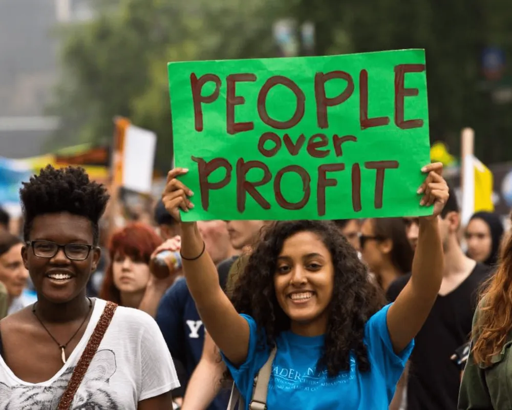 Young people at climate march, one of whom is holding a sign saying 'People over profit'