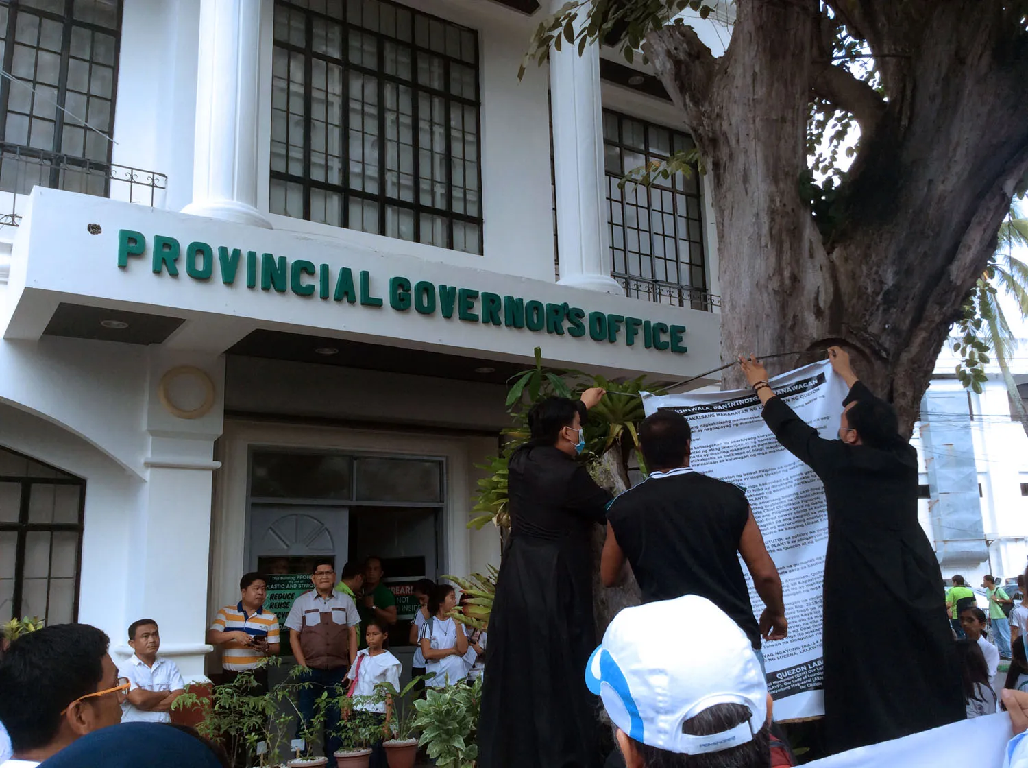 Priests and a community leader hang a blown-up copy of their demand letter to a tree in front of the provincial governor's office. Photo: Chuck Baclagon