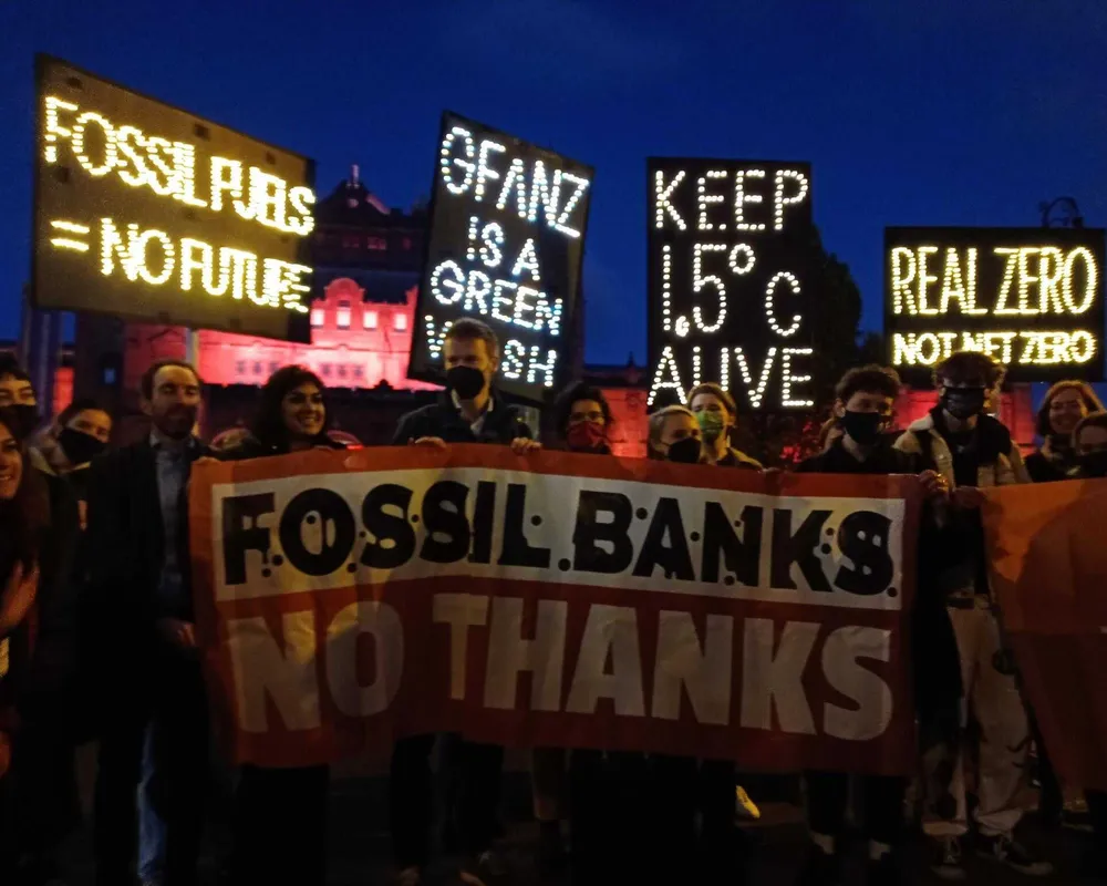 Activists hold signs protesting fossil finance outside COP26