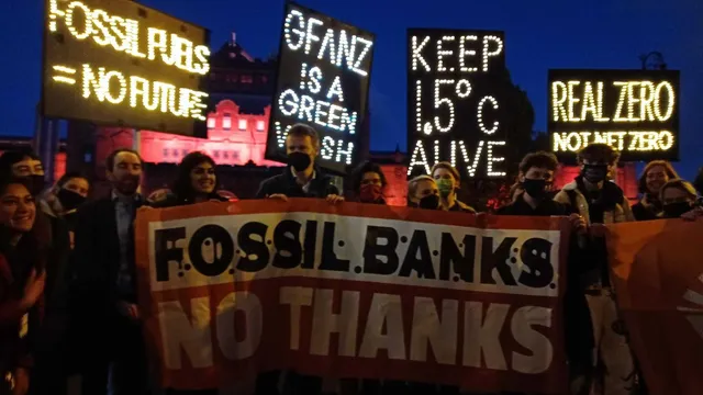 Activists hold signs protesting fossil finance outside COP26