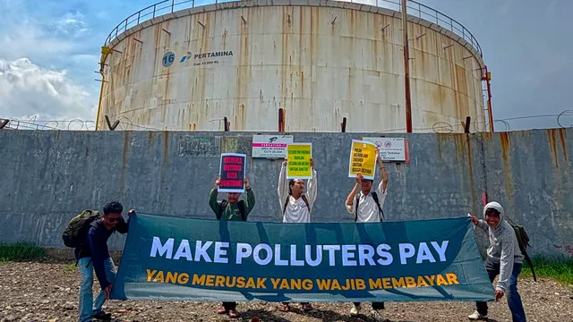 Activists stand in front of an oil plant, asking a phase out of fossil fuels