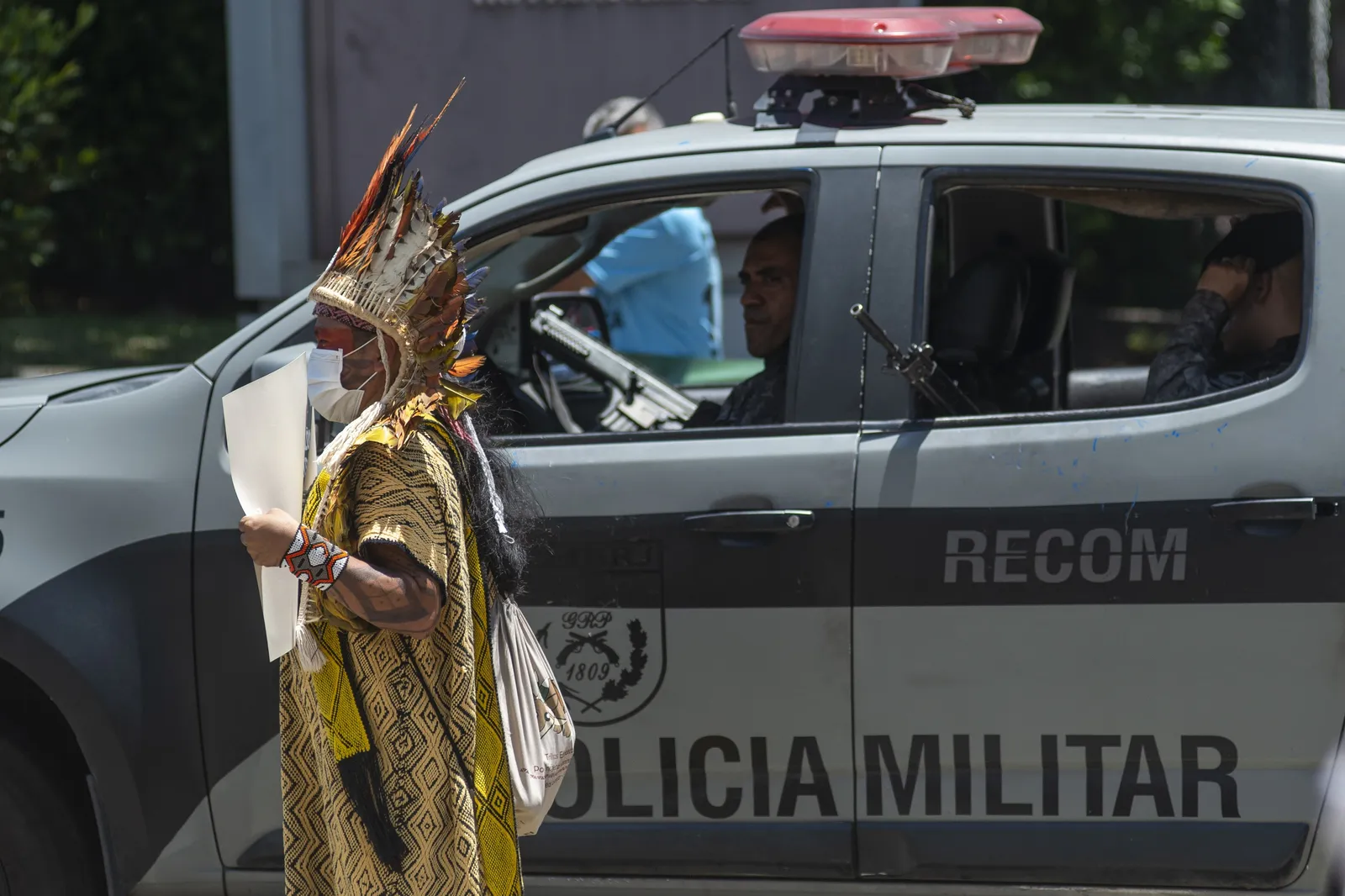 Cacique Ninawa Huni Kui in a pacific protest asking for no pollution in his land while the policemen looking to him with a gun.