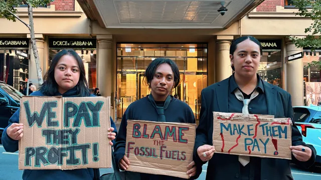 People standing in front of a bank with 'make them pay' posters