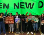 Group of activists holding protest signs and banners with "Green New Deal" message in green and white. Diverse crowd of young people advocating for climate action and environmental policy change.