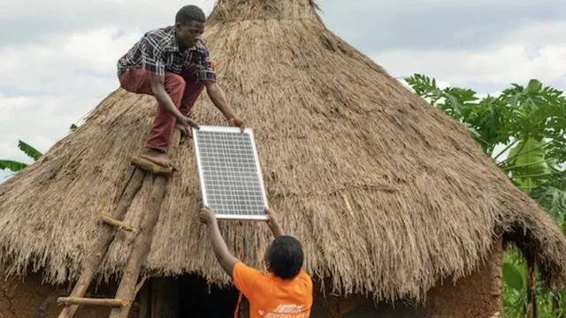 A solar panel being installed on a rooftop of a mud home.