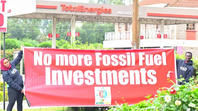 Aktivist*innen halten einen Banner auf dem "No more Fossil Fuel Investments" steht. Im Hintergrund ist eine Tankstelle von TOTAL zu sehen.