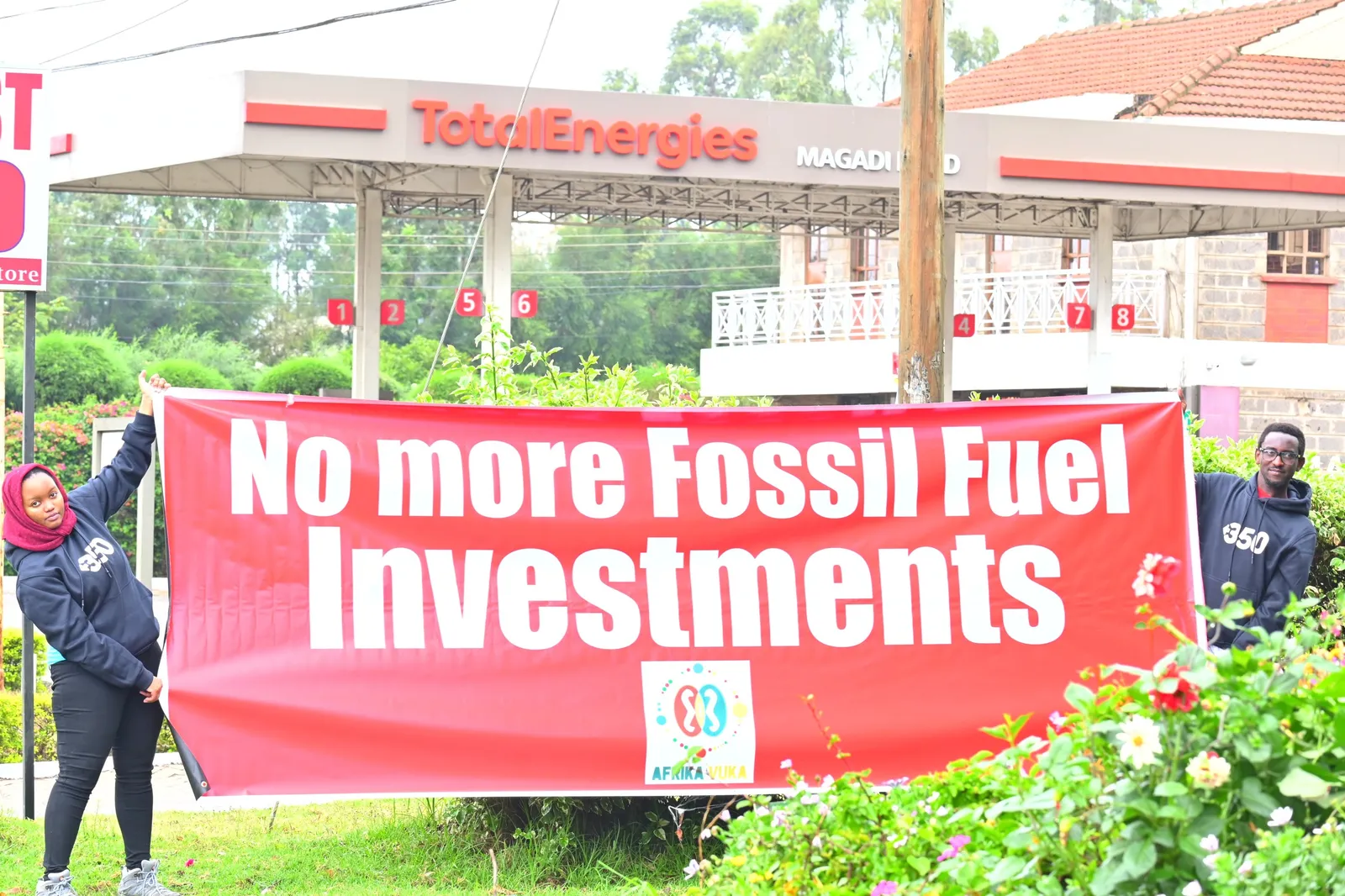 Aktivist*innen halten einen Banner auf dem "No more Fossil Fuel Investments" steht. Im Hintergrund ist eine Tankstelle von TOTAL zu sehen.