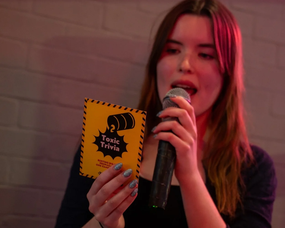 Toxic Trivia potrait of person speaking into microphone holding trivia card