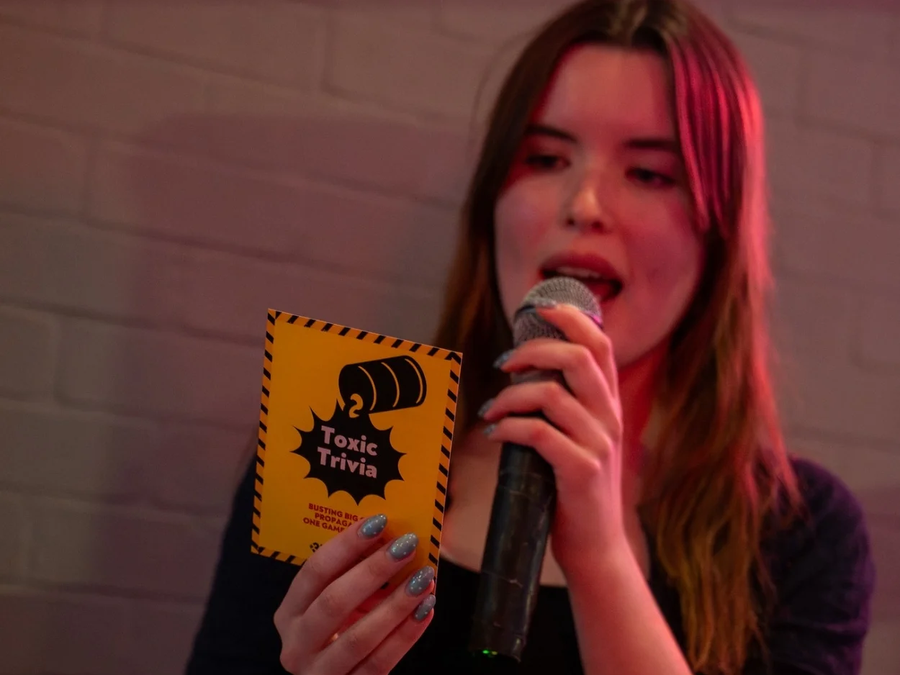 Toxic Trivia potrait of person speaking into microphone holding trivia card