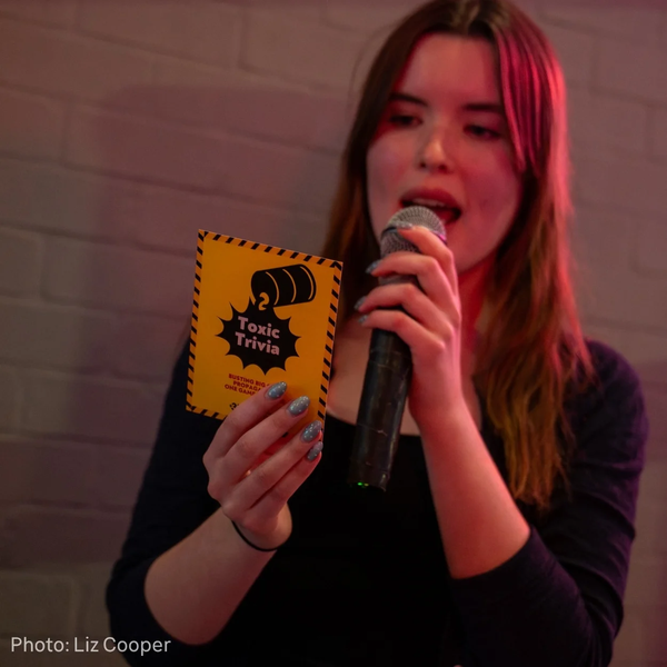 Toxic Trivia potrait of person speaking into microphone holding trivia card