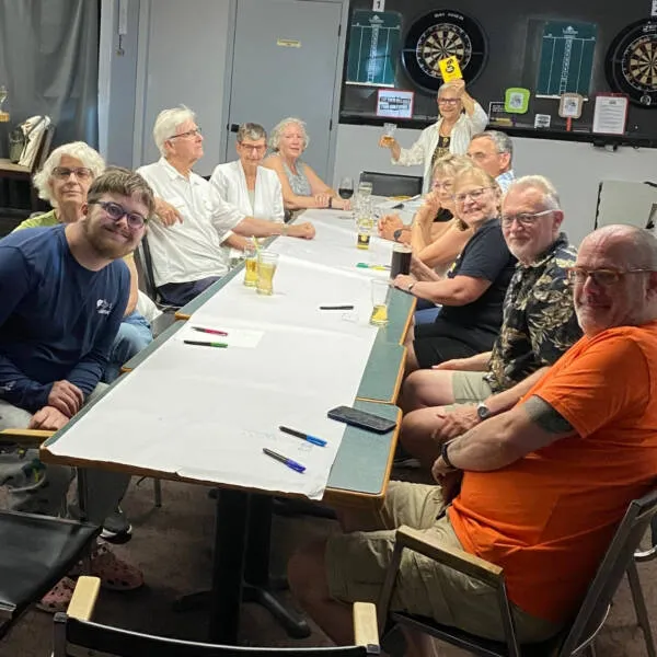 Toxic Trivia game night - people sitting around a table with a large sheet of paper across the entire table length playing