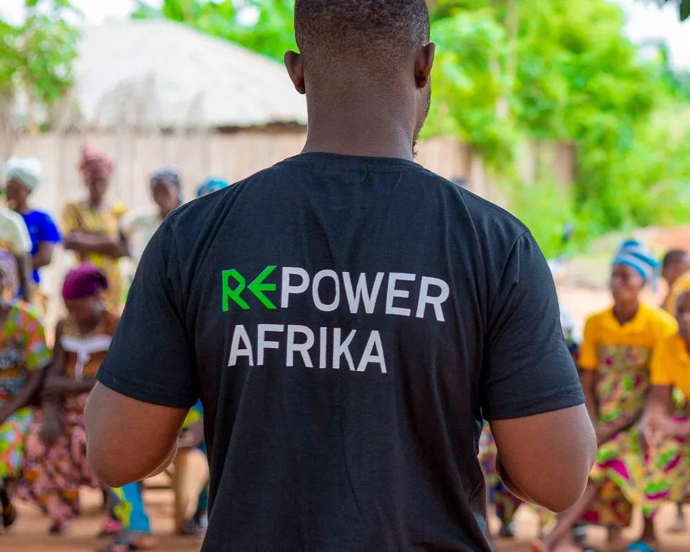 Activist wearing a "POWER AFRIKA" t-shirt talks to a community in an African village.