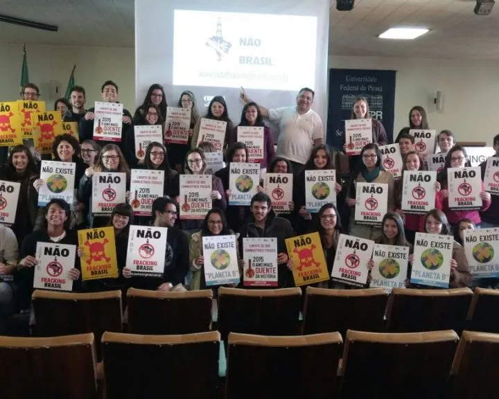Large group of activists holding protest signs with "NÃO" (NO) messages in Portuguese, gathered indoors for what appears to be an environmental or social campaign event.