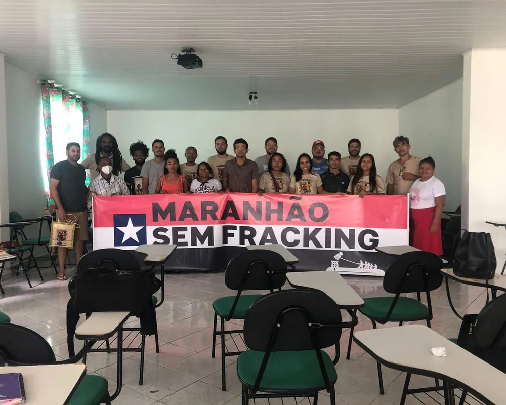 A group of people in a classroom holding a banner that reads "MARANHAO SEM FRACKING" (Maranhao Without Fracking) with a star symbol, advocating against hydraulic fracturing in the Brazilian state of Maranhao.