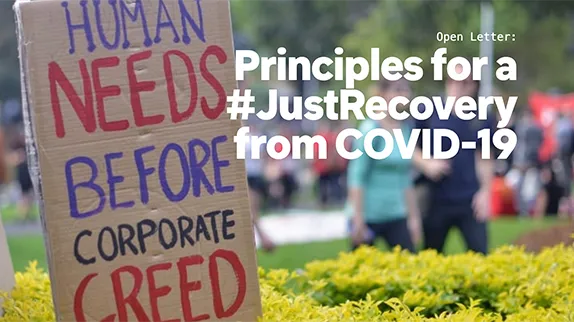 A sign reads human needs before corporate greed with a title saying Principles for a Just Recovery from COVID-19