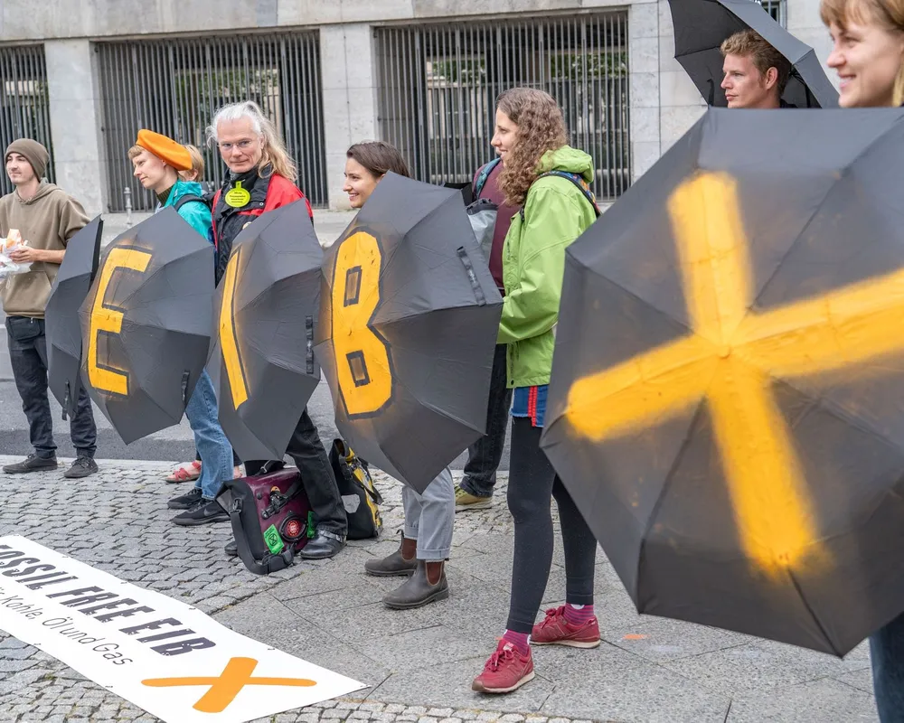People carrying black umbrellas reading EIB as part of the fossil free EIB campaign aimed at ending fossil finance