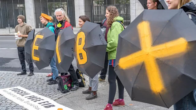 People carrying black umbrellas reading EIB as part of the fossil free EIB campaign aimed at ending fossil finance