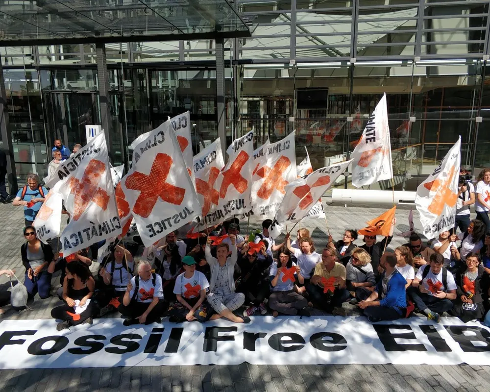 Group of activists outside European Investment Bank headquarters carrying banners and flags calling for an end to fossil fuel finance
