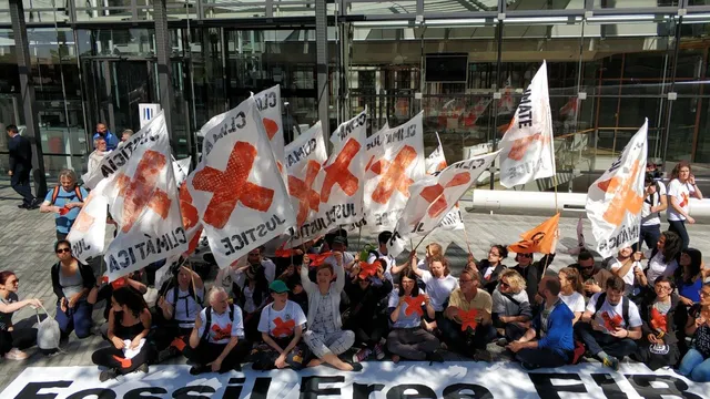 Group of activists outside European Investment Bank headquarters carrying banners and flags calling for an end to fossil fuel finance
