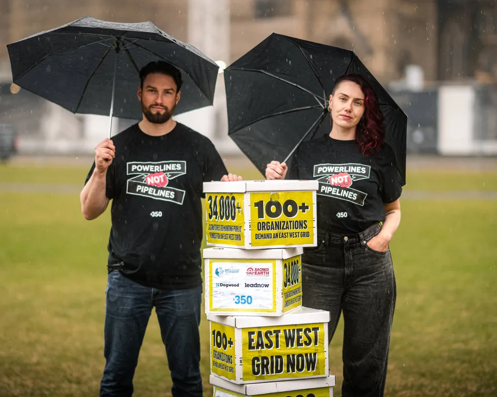 Powerlines not pipelines - 2 people standing in the rain  holding umbrellas delivering boxes of petition signers