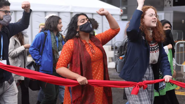 A woman in an orange sari is holding a red line, fist raised, during the final day of COP26