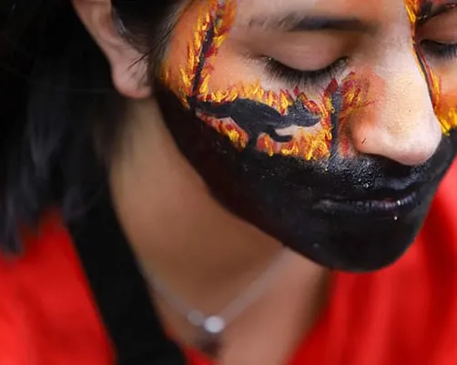 Close up of a young woman with her face painted with fire and the silhouette of a kangaroo.