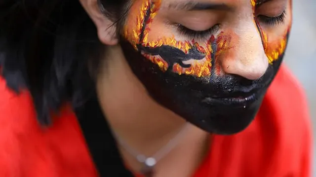 Close up of a young woman with her face painted with fire and the silhouette of a kangaroo.