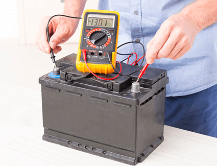 A car battery is being tested with a multimeter