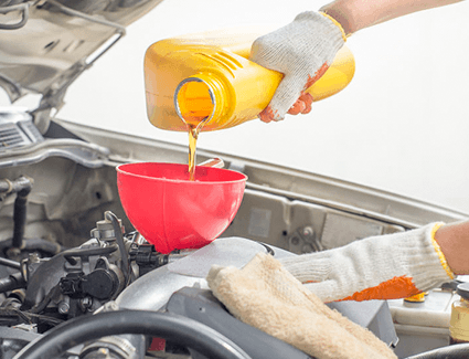 Using gloves and a funnel, a technician completes an oil change service on this vehicle by pouring oil into the engine