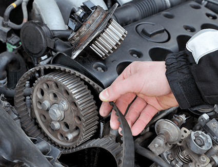 Hand removing timing belt from engine and water pump sitting on top of valve cover