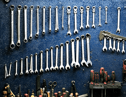 A variety of wrenches and other tools hanging on a wall.