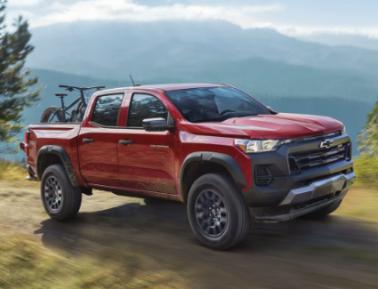 ¾ exterior view of a Radiant Red Tintcoat driving on a dirt road.