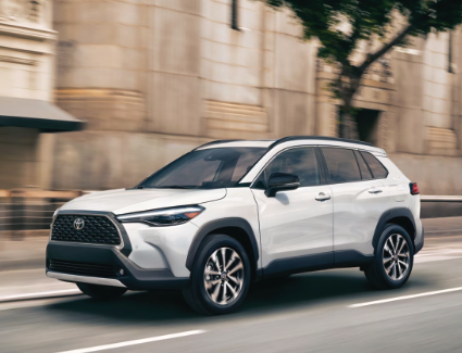 Exterior view of a white 2025 Corolla Cross driving down the street