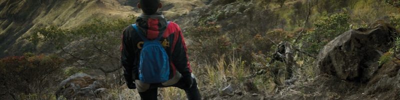 man in blue jacket and black pants standing on rock mountain during daytime