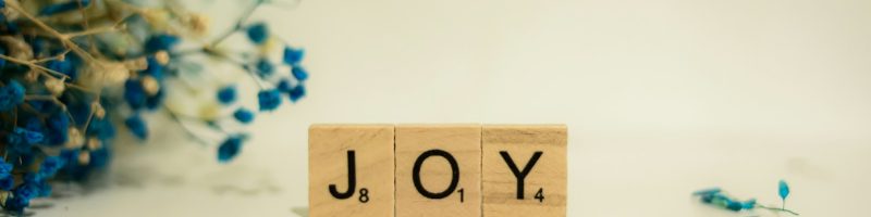 a wooden block that says joy next to a bouquet of flowers